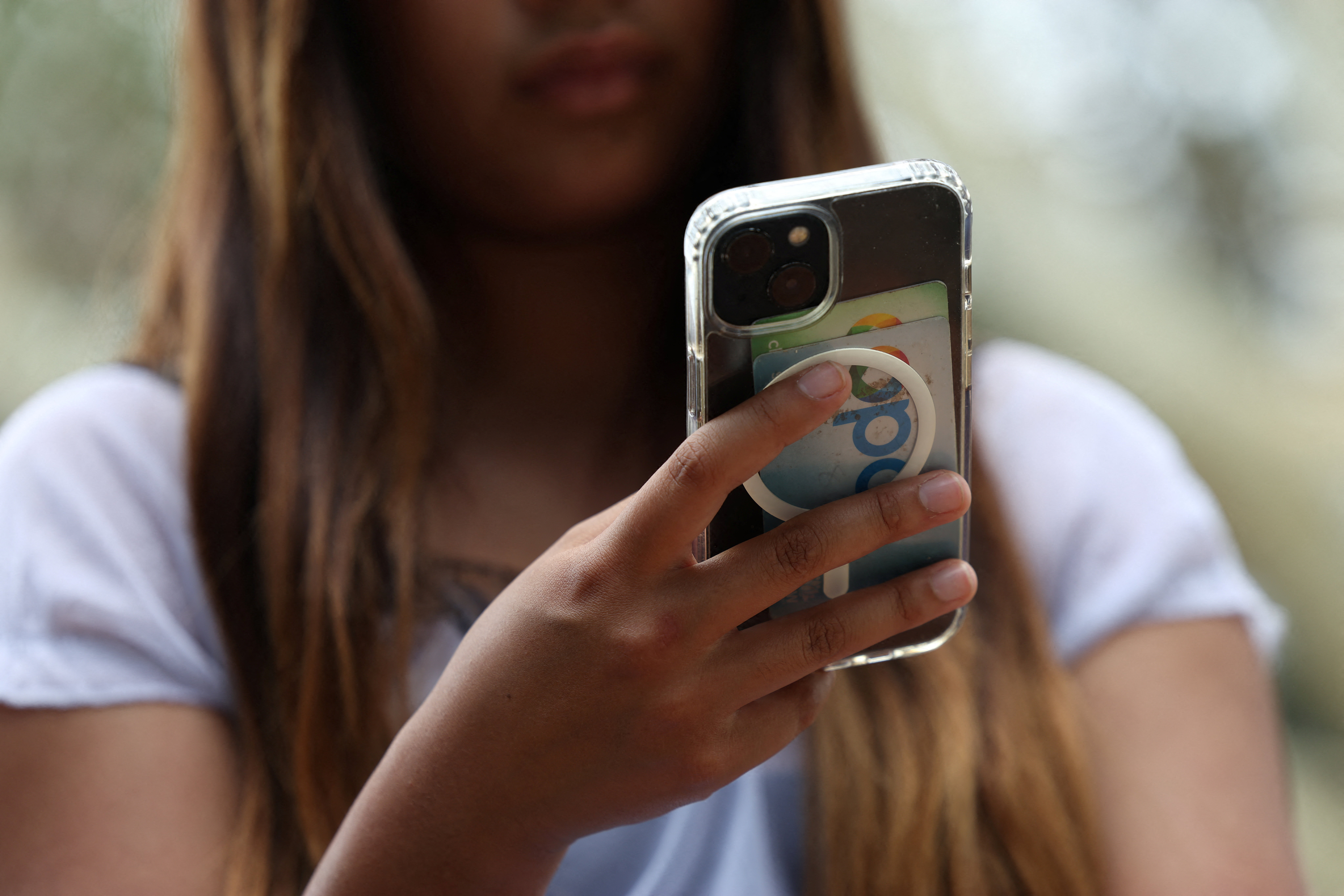 A teenager poses holding a mobile phone as law banning social media for users under 16 in Australia takes effect, in Sydney