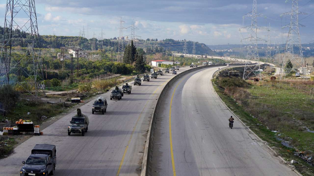 Military vehicles drive along a road in Latakia