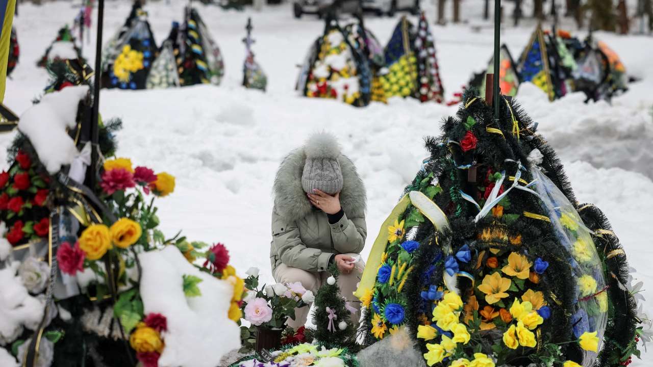 A woman reacts as she sits in front of a grave at a local cemetery, decorated with flowers to pay tribute to the victims of the Russian attack on Ukraine, in Chernihiv