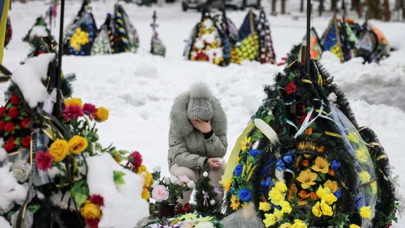 A woman reacts as she sits in front of a grave at a local cemetery, decorated with flowers to pay tribute to the victims of the Russian attack on Ukraine, in Chernihiv