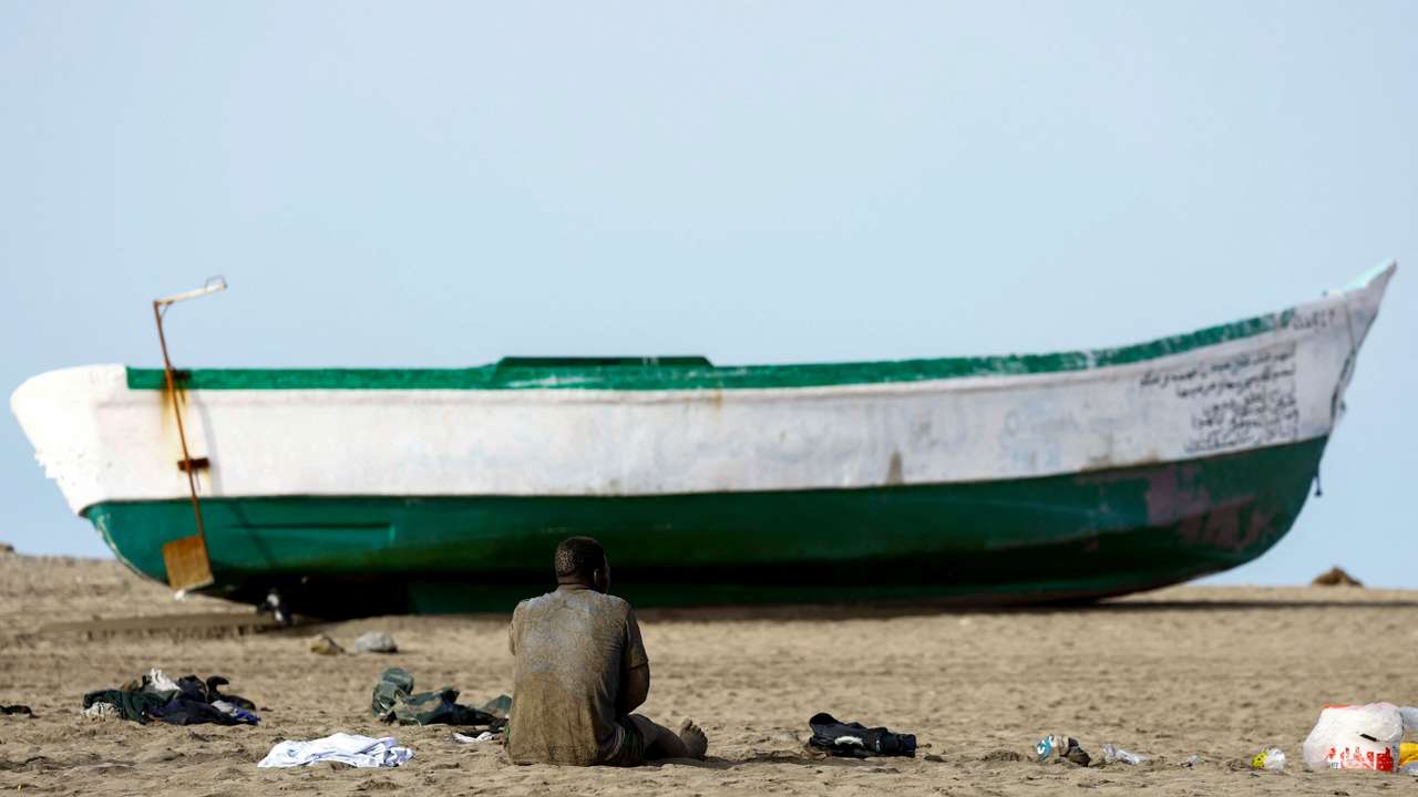A migrant rests sitting on the sand next to the fiber boat in which he arrived at Las Burras Beach in San Agustin