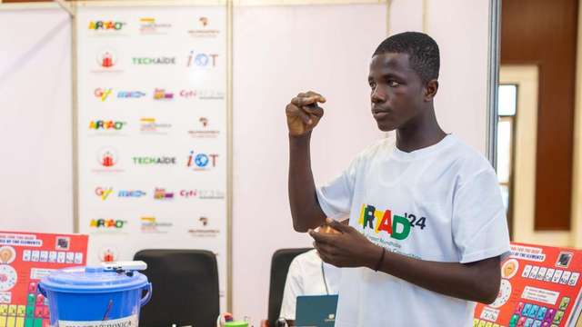 Thomas Djabatey in front of his team's booth talking about the Smart Periodic Table at the Robotics Competition in Accra