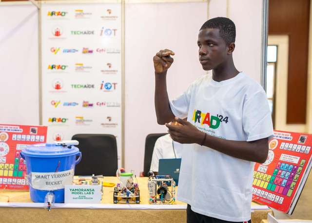 Thomas Djabatey in front of his team's booth talking about the Smart Periodic Table at the Robotics Competition in Accra