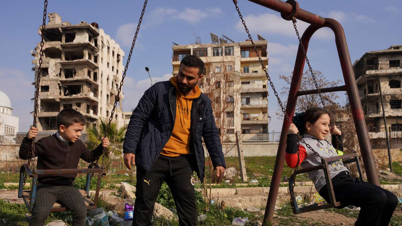 Syrian Ahmed Al-Sheikh, who returned to his homeland from neighbouring Turkey after the fall of Bashar al-Assad, plays with his children at a park near damaged buildings in Aleppo