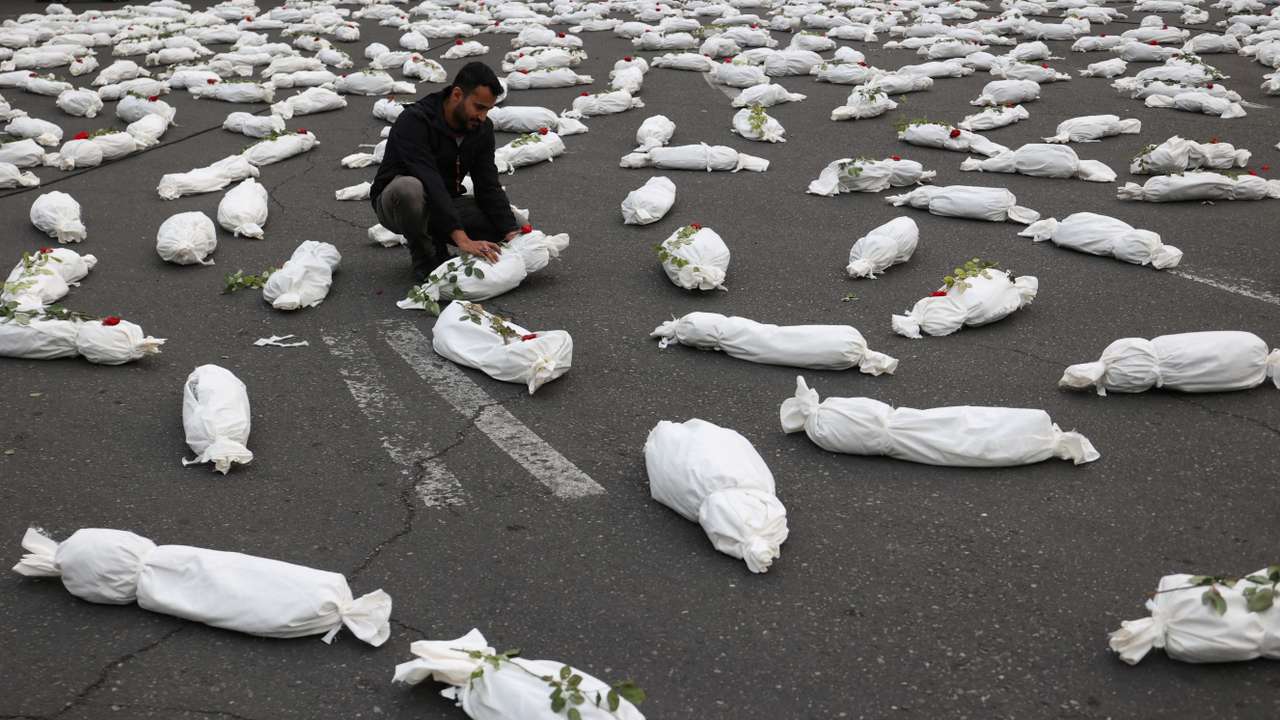 An Iranian man sits next to the symbolic shrouds of Gaza children's dead bodies during a gesture in a street in Tehran