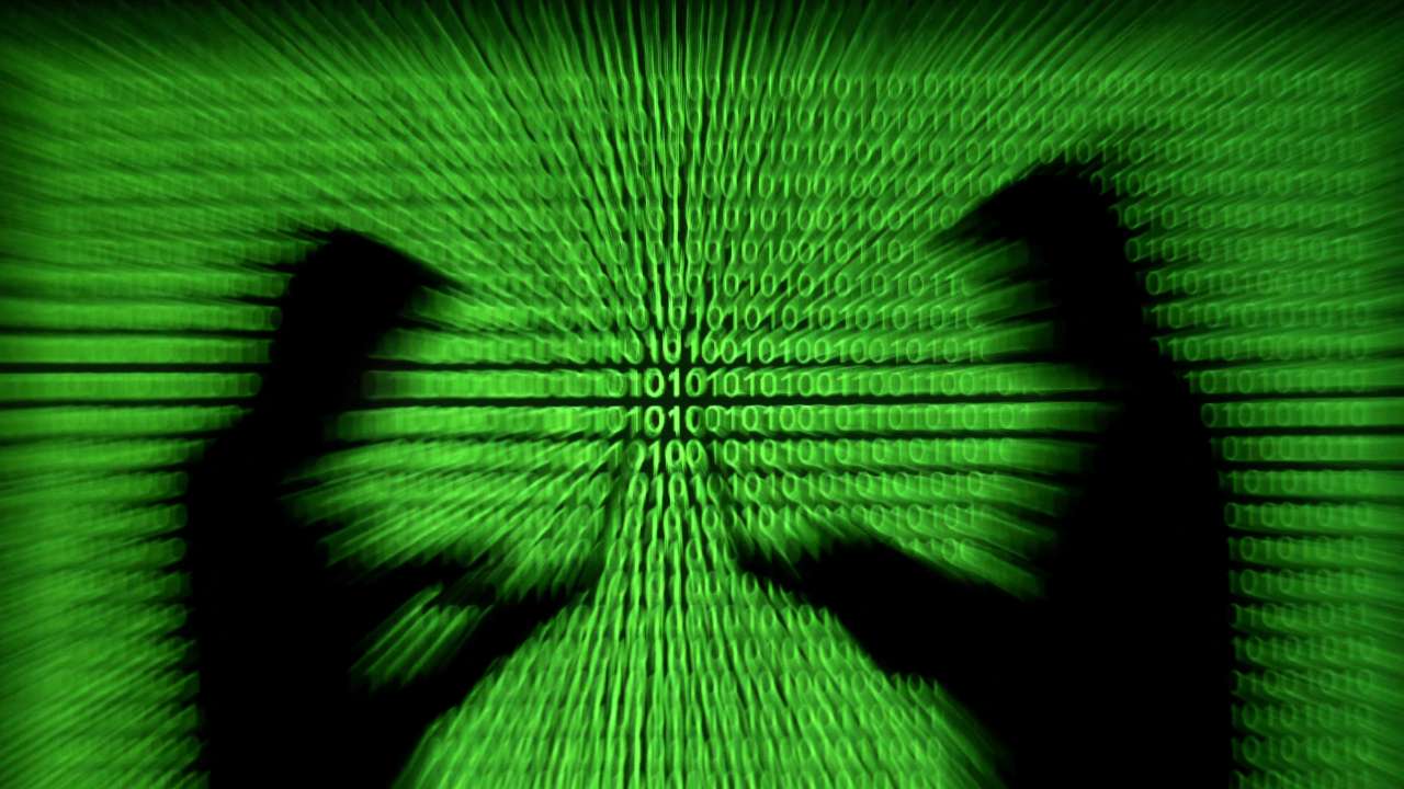 FILE PHOTO: Silhouettes of laptop users are seen next to a screen projection of binary code are seen in this picture illustration