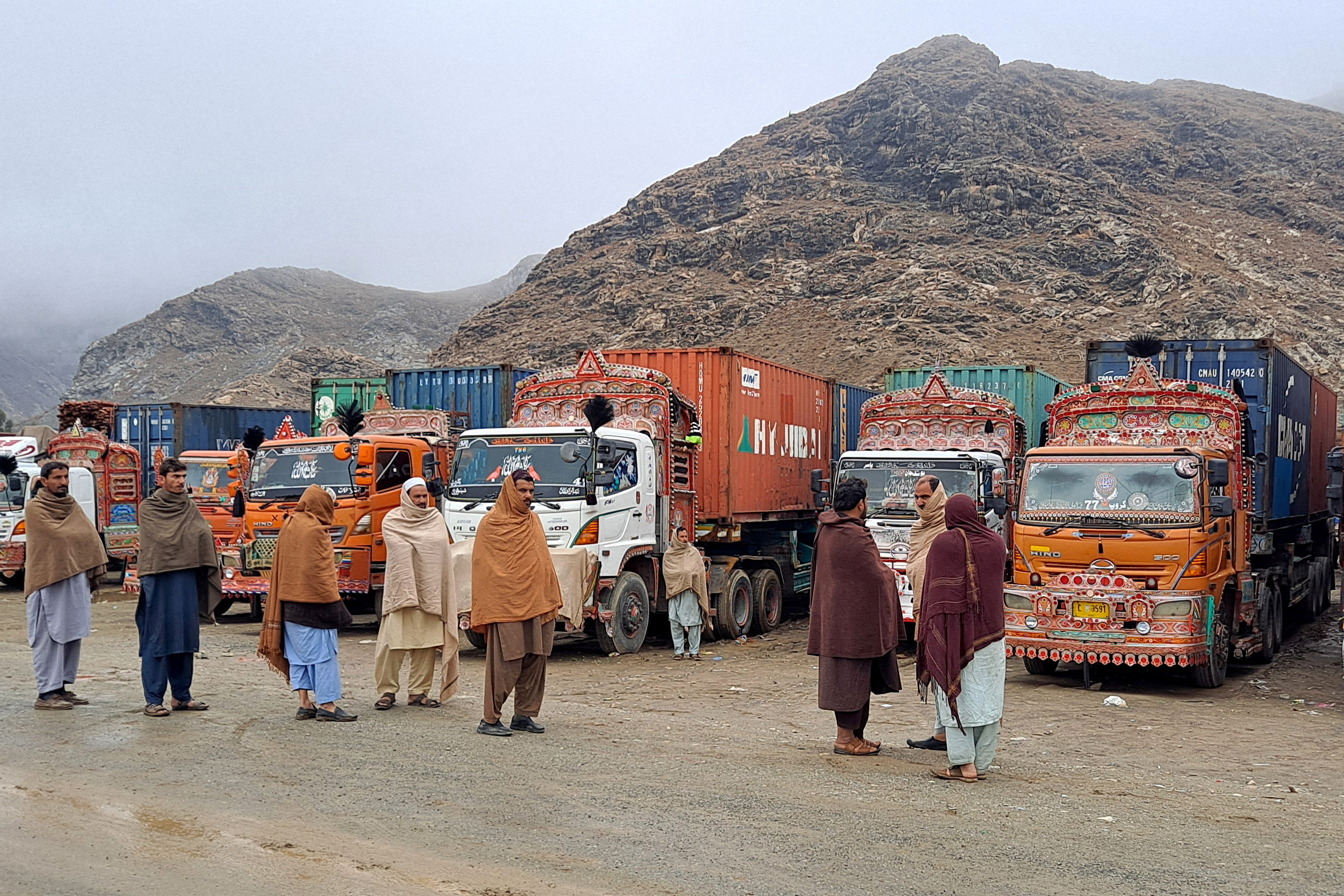 People stand next to parked trucks loaded with supplies at the Torkham border