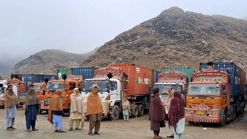 People stand next to parked trucks loaded with supplies at the Torkham border
