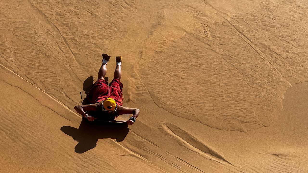 A tourist sandboards on the dunes in Walvis Bay
