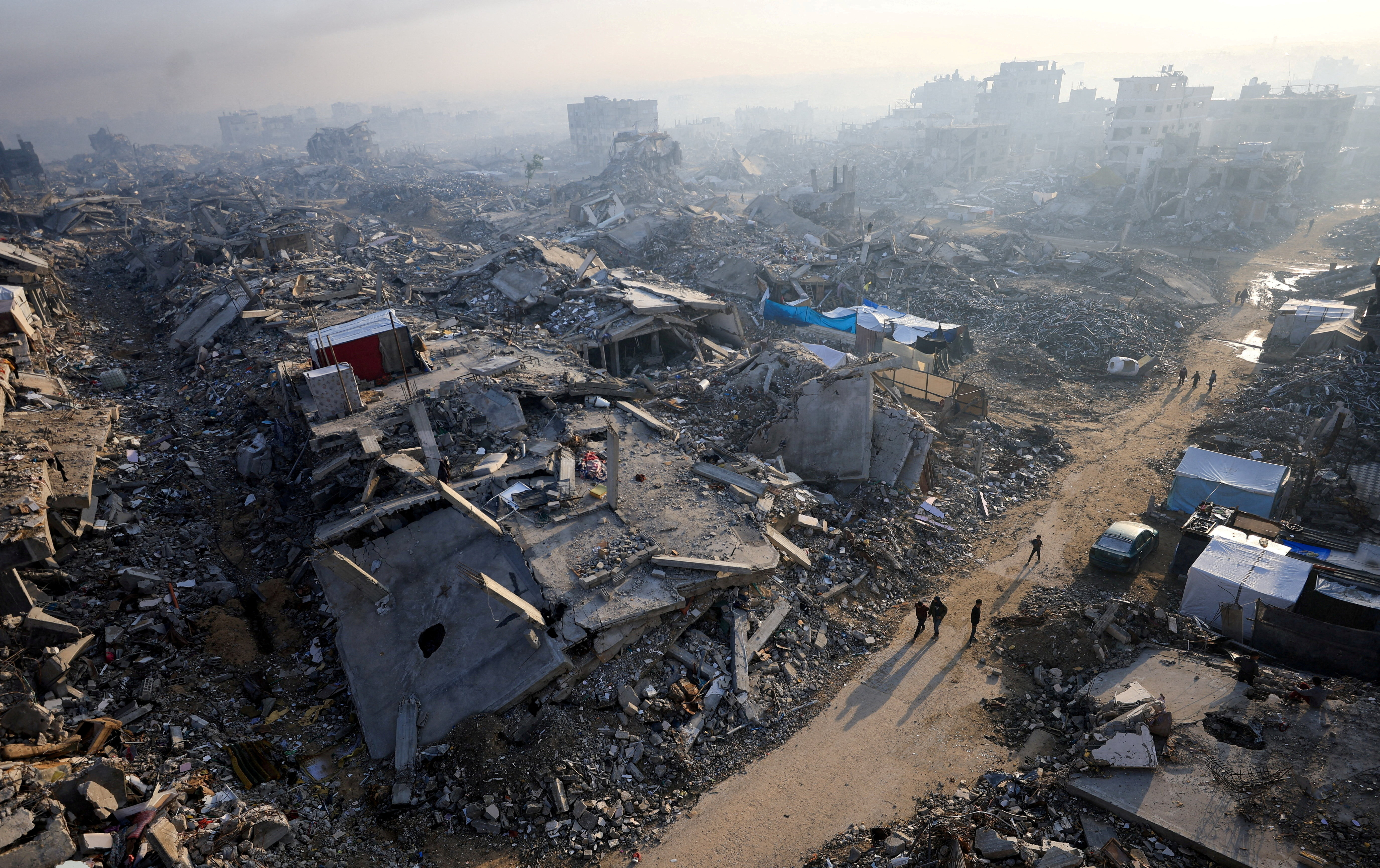 FILE PHOTO: Palestinians walk past the rubble of destroyed buildings, in Gaza City