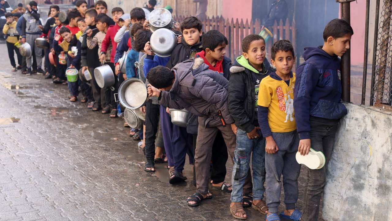 Palestinian children carry pots as they queue to receive food cooked by a charity kitchen, in Rafah in the southern Gaza Strip
