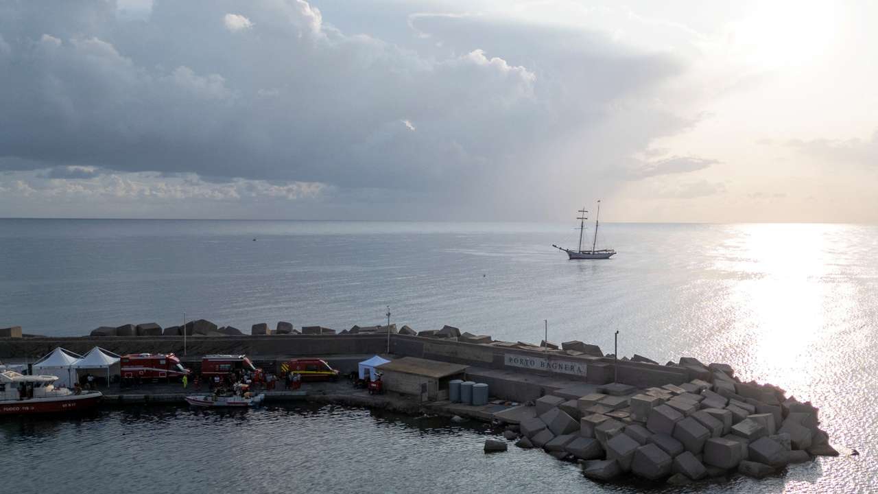 Rescue service vehicles and personnel at a port near the site where a luxury yacht sank, in Porticello