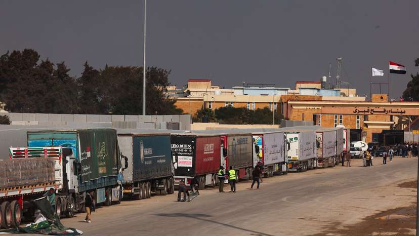 People stand next to trucks carrying humanitarian aid, at the Rafah border crossing to enter Gaza