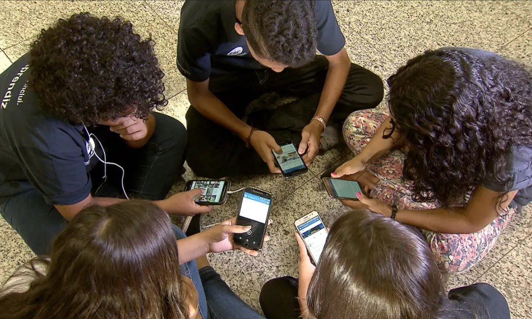 Adolescentes reunidos em uma roda utilizando celulares