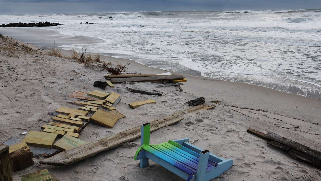 A chair lays on the sand with other debris as waves rush the beach during the pass of a winter storm in Lido beach, New York