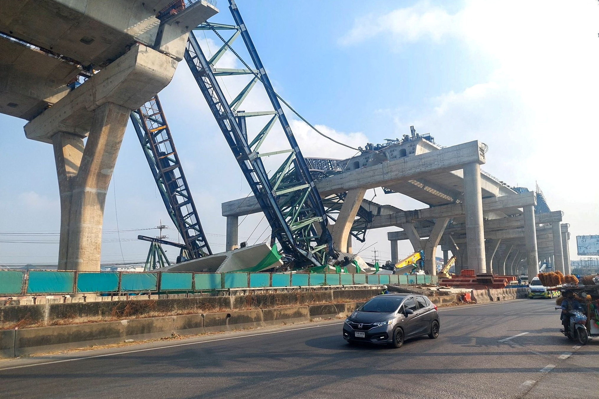 Cars drive next to a collapsed crane that crushed two vehicles during construction of an elevated highway in Samut Sakhon province