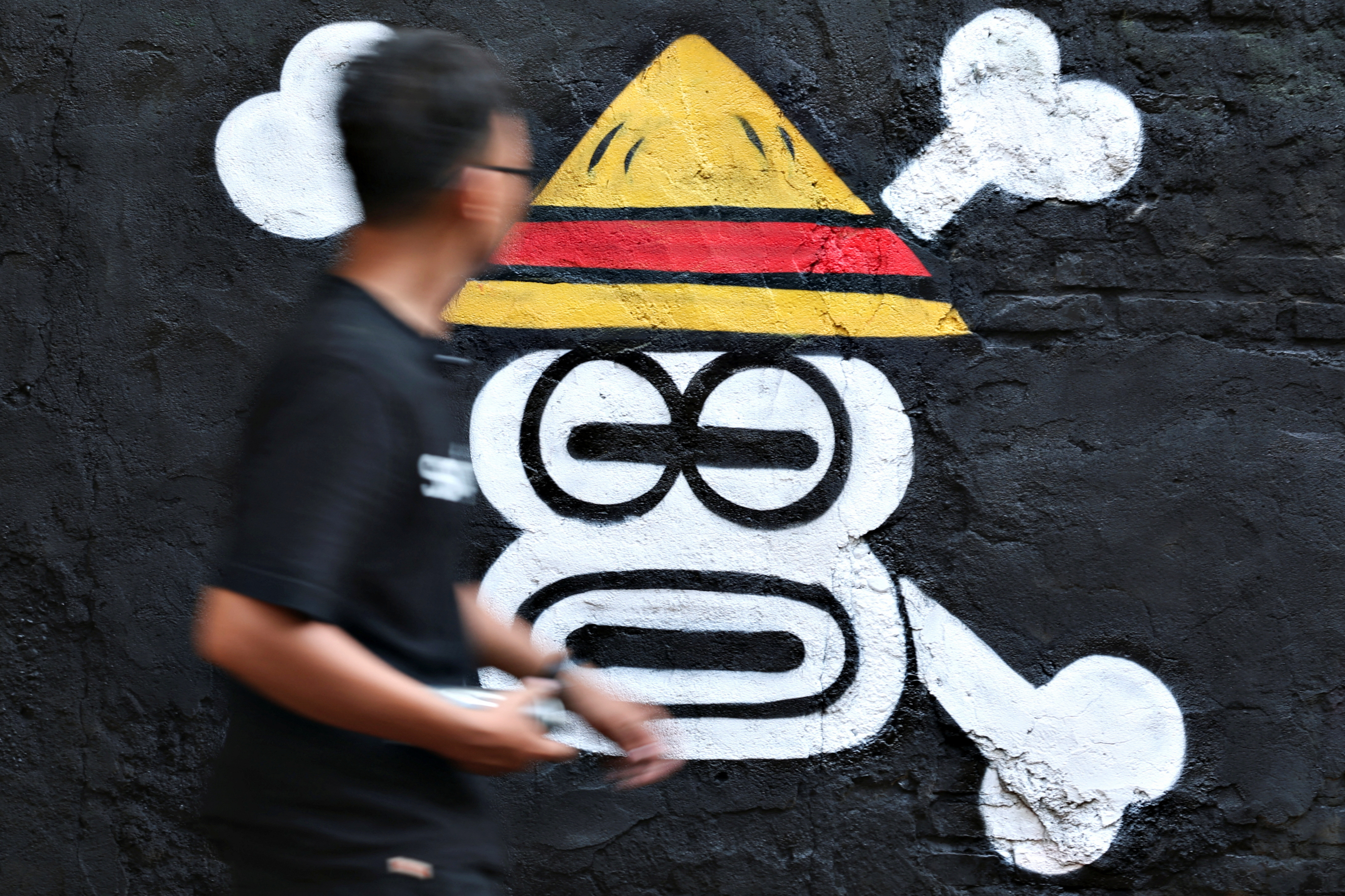 Kemas Muhammad Firdaus, 28, walks past a mural depicting a Jolly Roger from the popular Japanese anime and manga series 'One Piece' in Bekasi