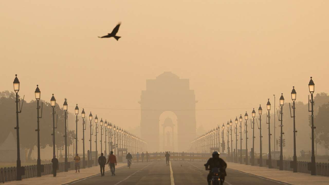 People walk on Kartavyapath near India Gate on a hazy morning in New Delhi