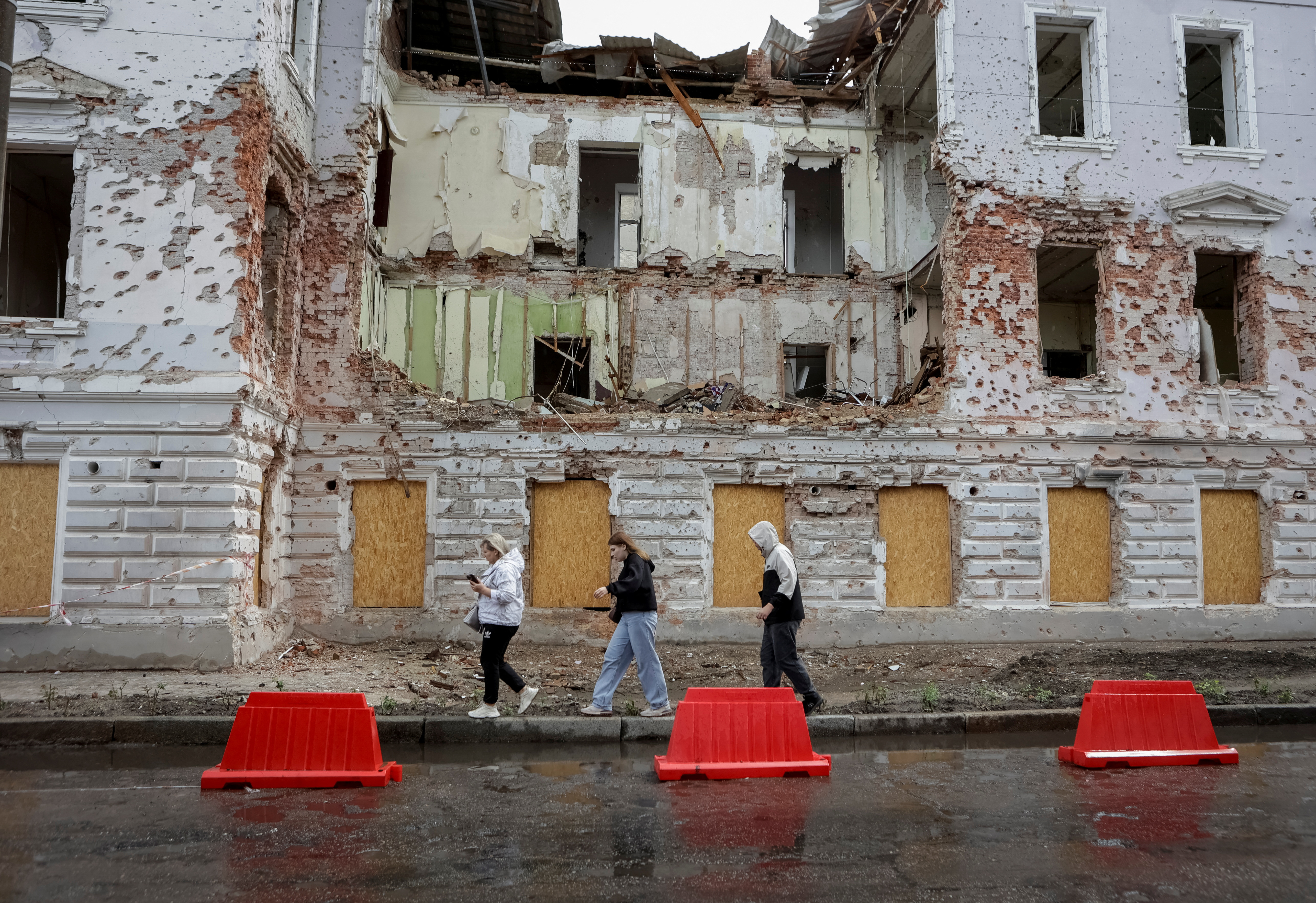Residents walk at a street near a building damaged by Russian missile strikes in Sumy