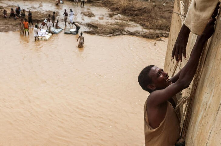 A survivor is being helped to climb a wall, following devastating floods, in South Tokar