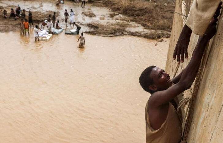 A survivor is being helped to climb a wall, following devastating floods, in South Tokar