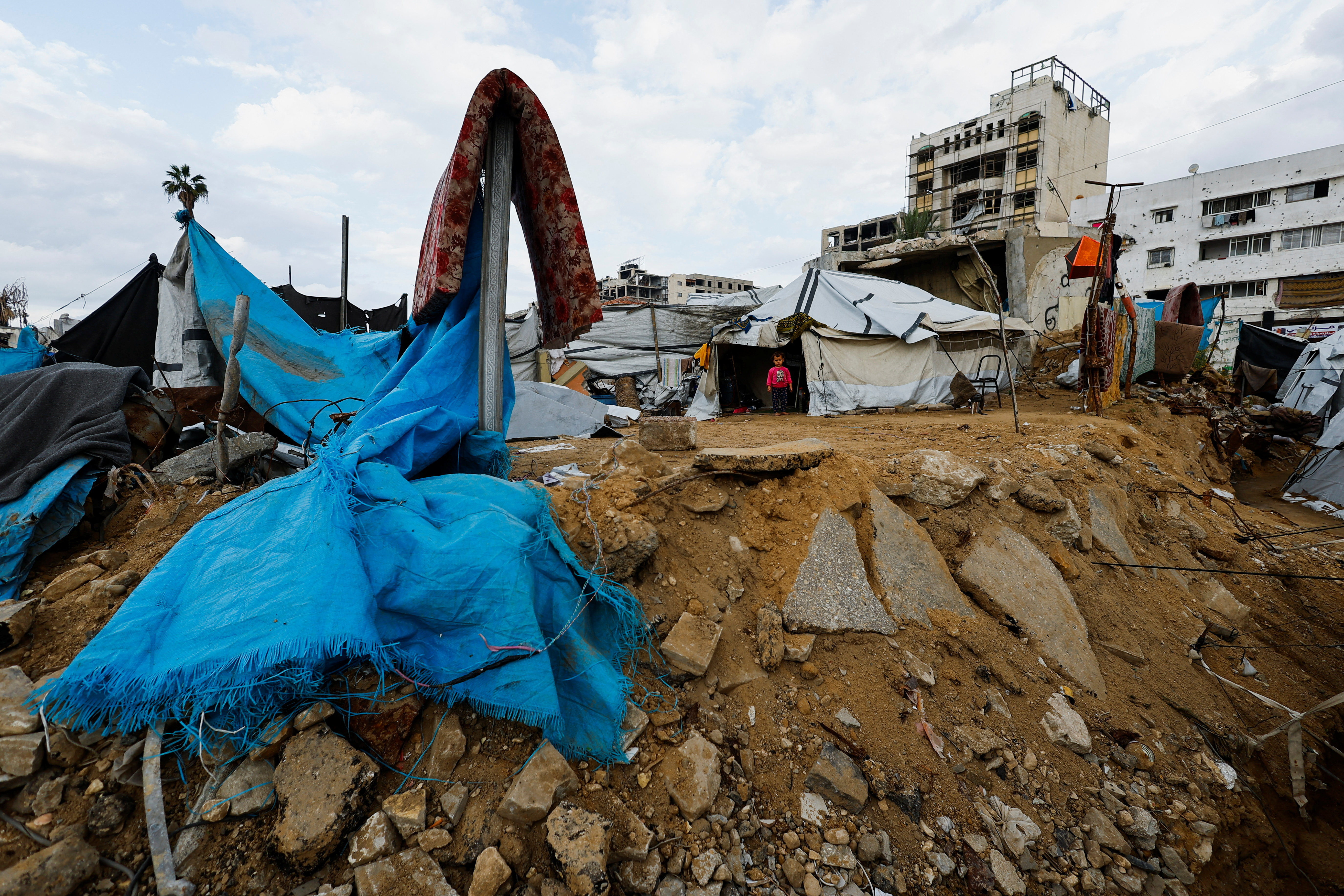 Palestinian child stands in front of a tent on a rainy day in Gaza City