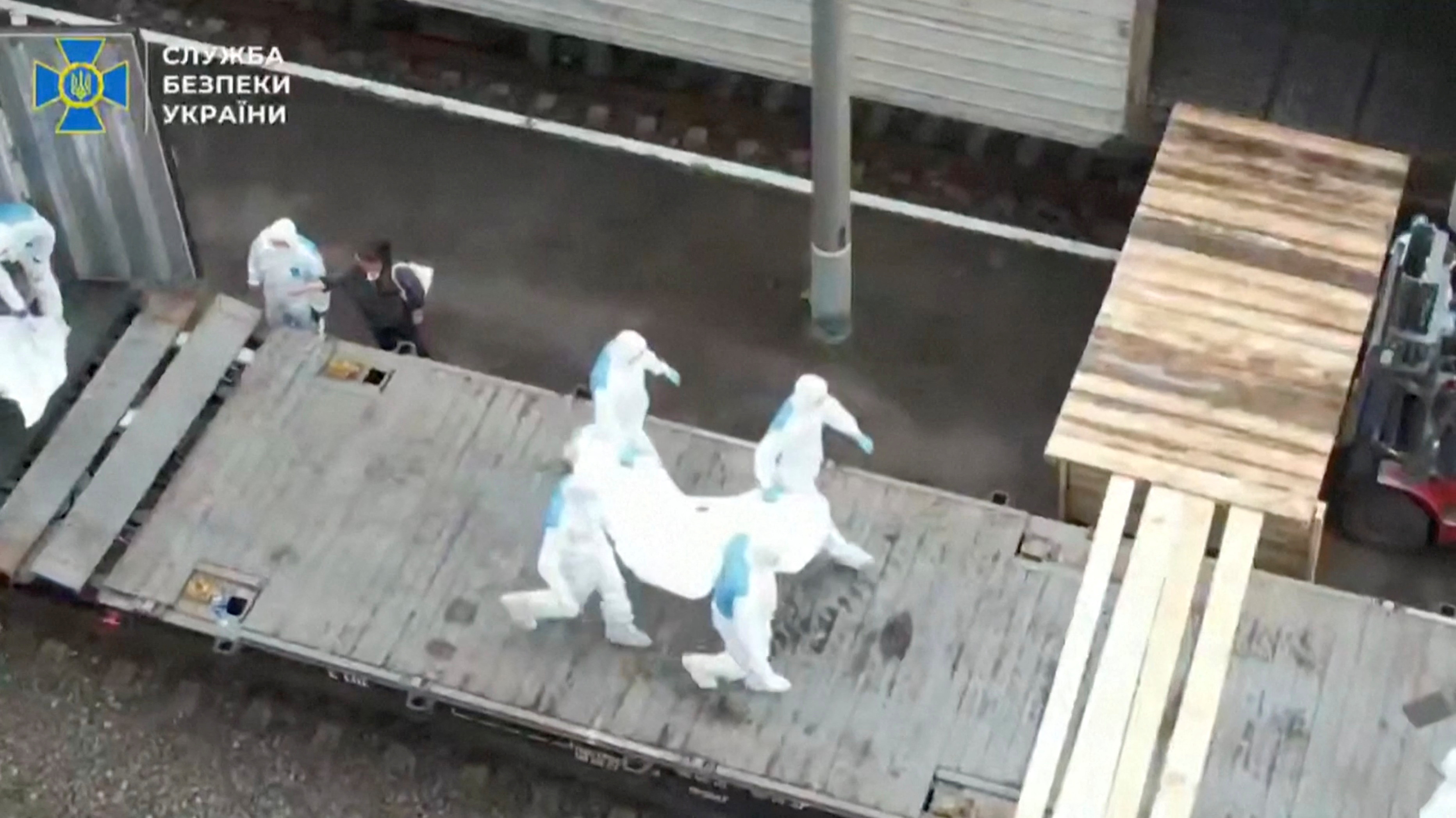 People in hazmat suits carry what is said to be remains of Ukrainian soldiers received from Russia in an unknown location
