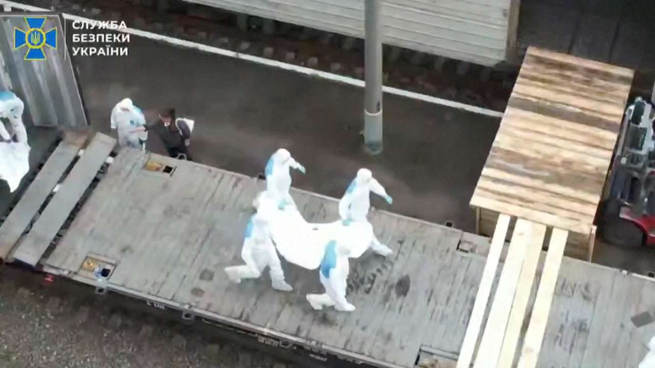 People in hazmat suits carry what is said to be remains of Ukrainian soldiers received from Russia in an unknown location