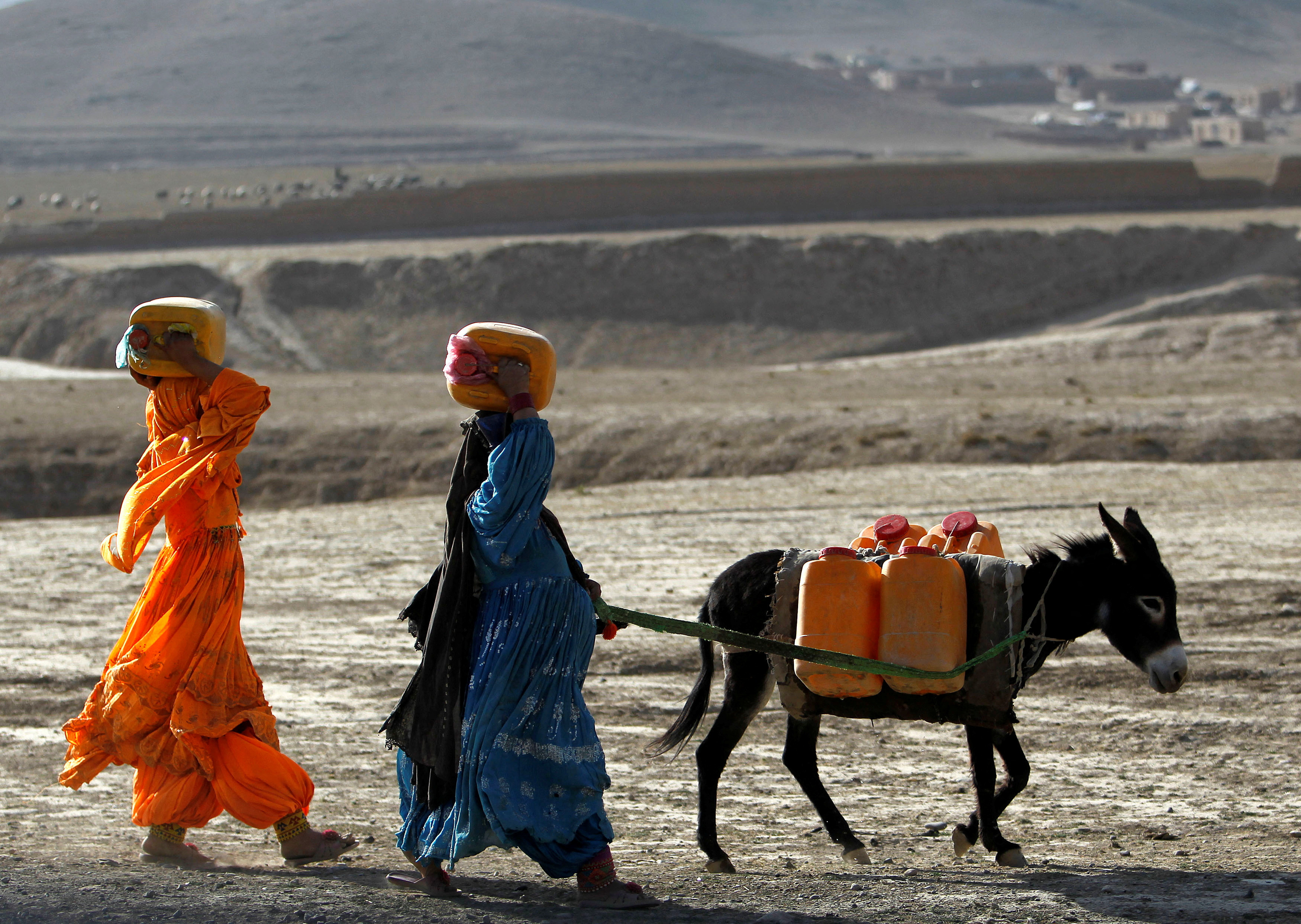 FILE PHOTO: Afghan kochi nomad women carry water containers on their heads
