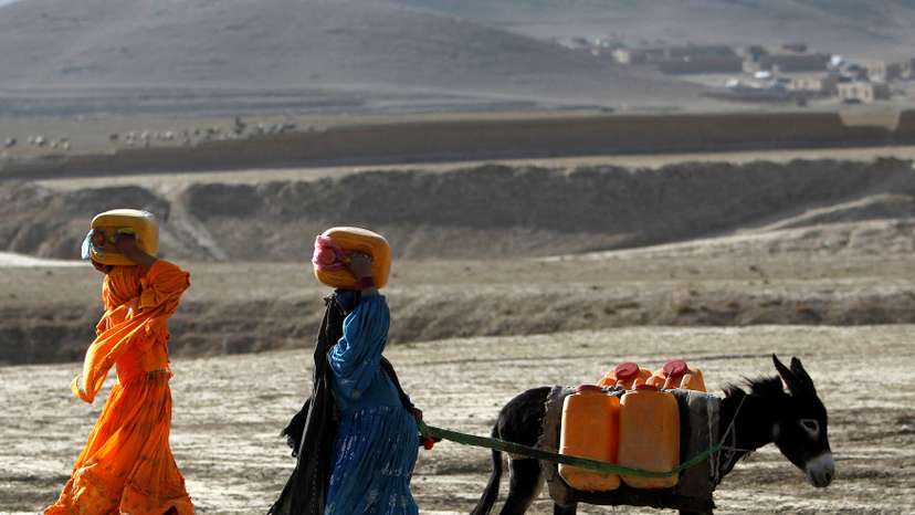 FILE PHOTO: Afghan kochi nomad women carry water containers on their heads