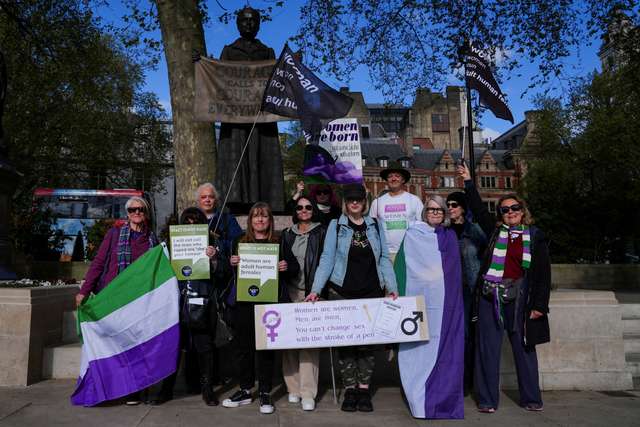 People hold signs as they await a ruling on an appeal by For Women Scotland on whether a person with a full Gender Recognition Certificate (GRC) recognising their gender as female is a woman under British equality laws, at Parliament Square in London, Britain, April 16, 2025. REUTERS/Maja Smiejkowska