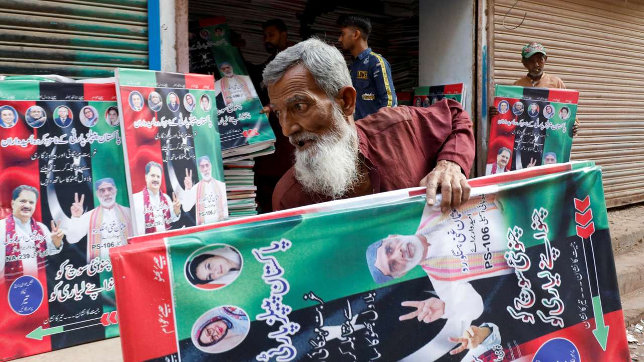 A worker carries campaign posters of a political party to decorate the area, ahead of general elections, in Karachi