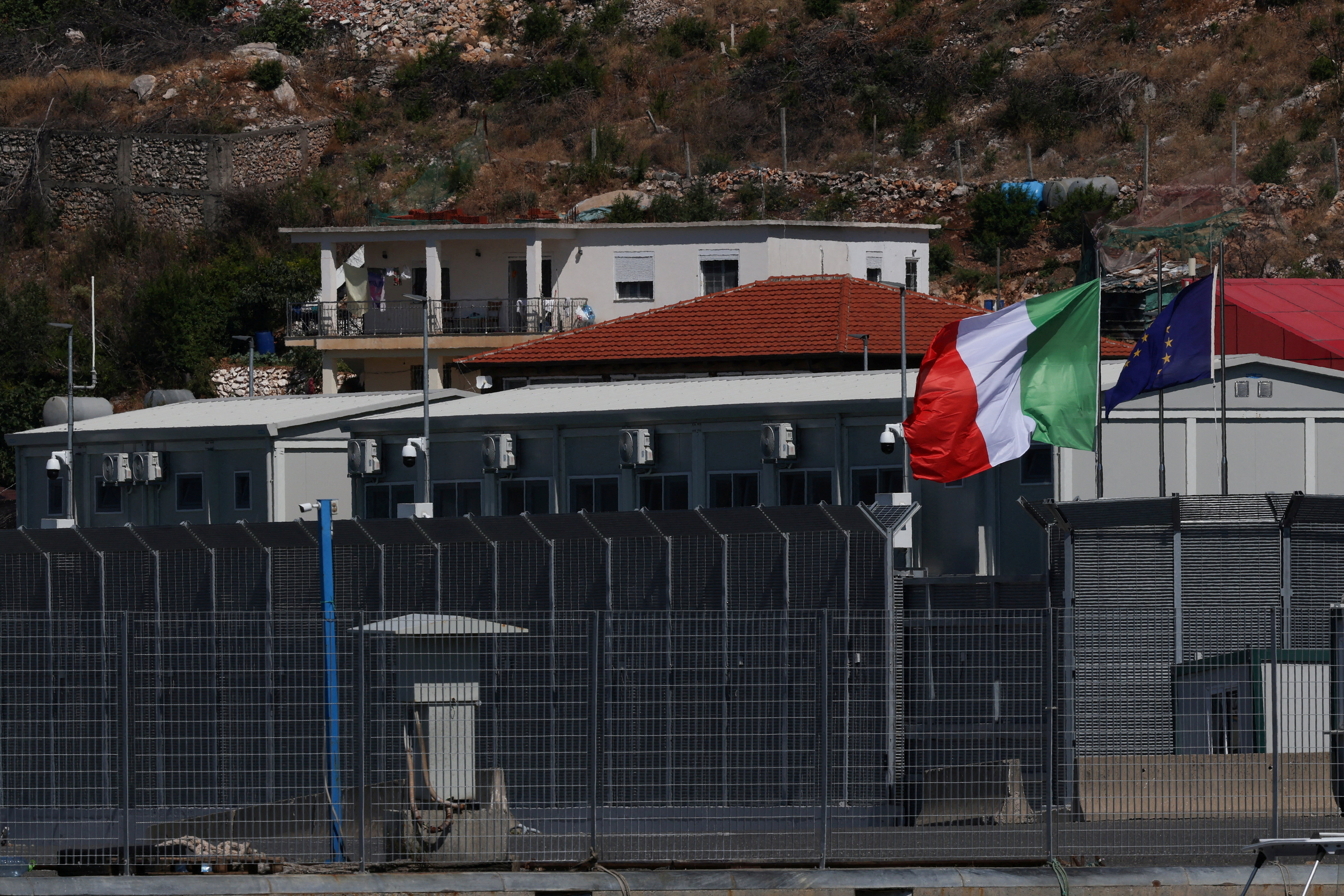 FILE PHOTO: Italian and European Union flags flutter at a reception camp to process migrants rescued at sea, in Shengjin