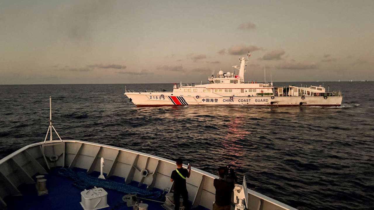 FILE PHOTO: Members of the media take footage of a Chinese Coast Guard vessel blocking a Philippine Coast Guard vessel on its way to a resupply mission at Second Thomas Shoal in the South China Sea
