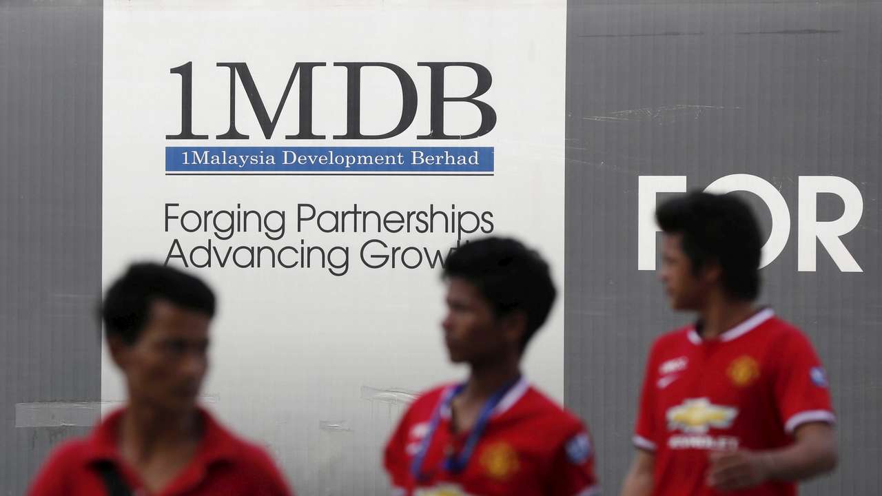 Men walk past a 1Malaysia Development Berhad (1MDB) billboard at the fund's flagship Tun Razak Exchange development in Kuala Lumpur