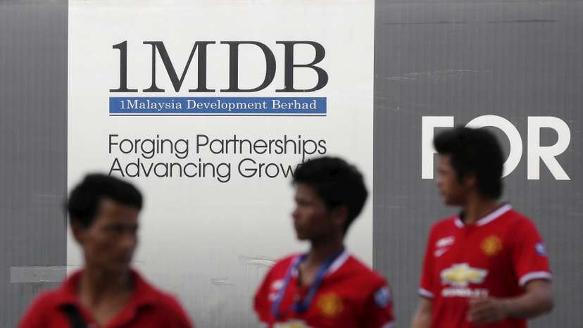 Men walk past a 1Malaysia Development Berhad (1MDB) billboard at the fund's flagship Tun Razak Exchange development in Kuala Lumpur