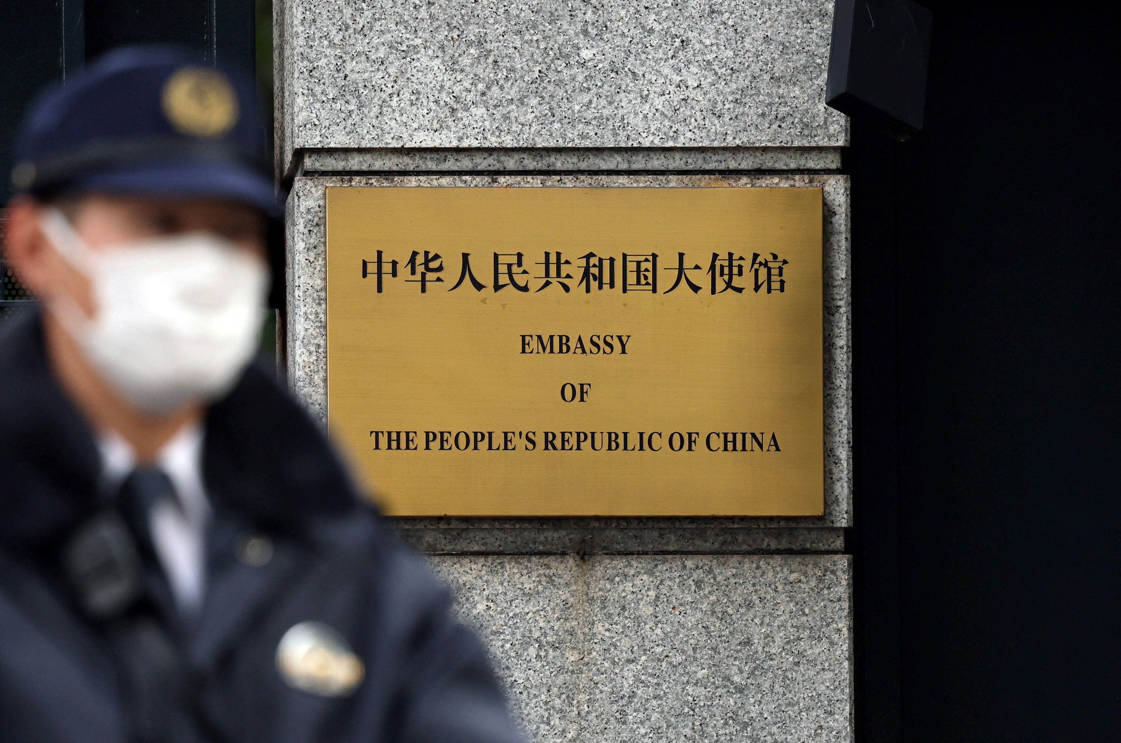 A Japanese police officer stands guard next to a plaque at the entrance of the Chinese embassy in Tokyo