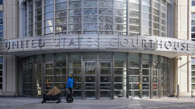 A person rides an electric unicycle while pulling a wagon loaded with packages, in front of the Eastern District of New York Court Federal Court House in New York City