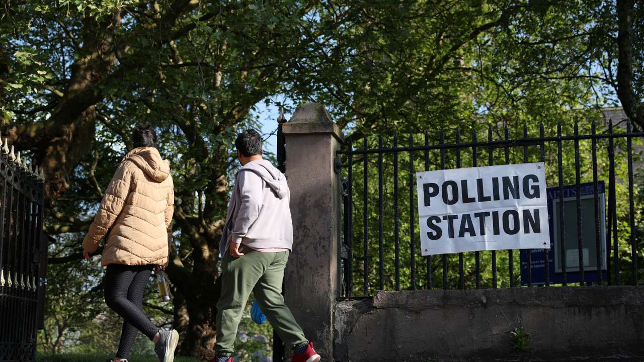 People walk past a polling station sign outside a church as voting gets underway in the Runcorn and Helsby parliamentary by-election in Runcorn, Britain