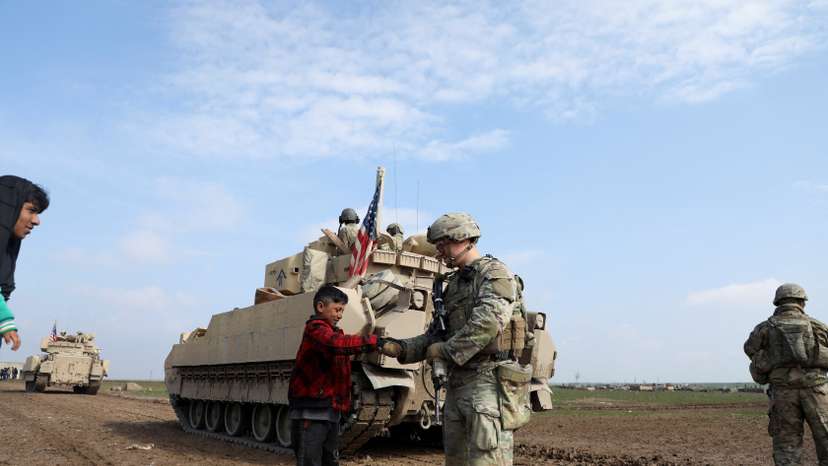 FILE PHOTO: A soldier from the US-led coalition holds the hand of a boy in the countryside of Qamishli