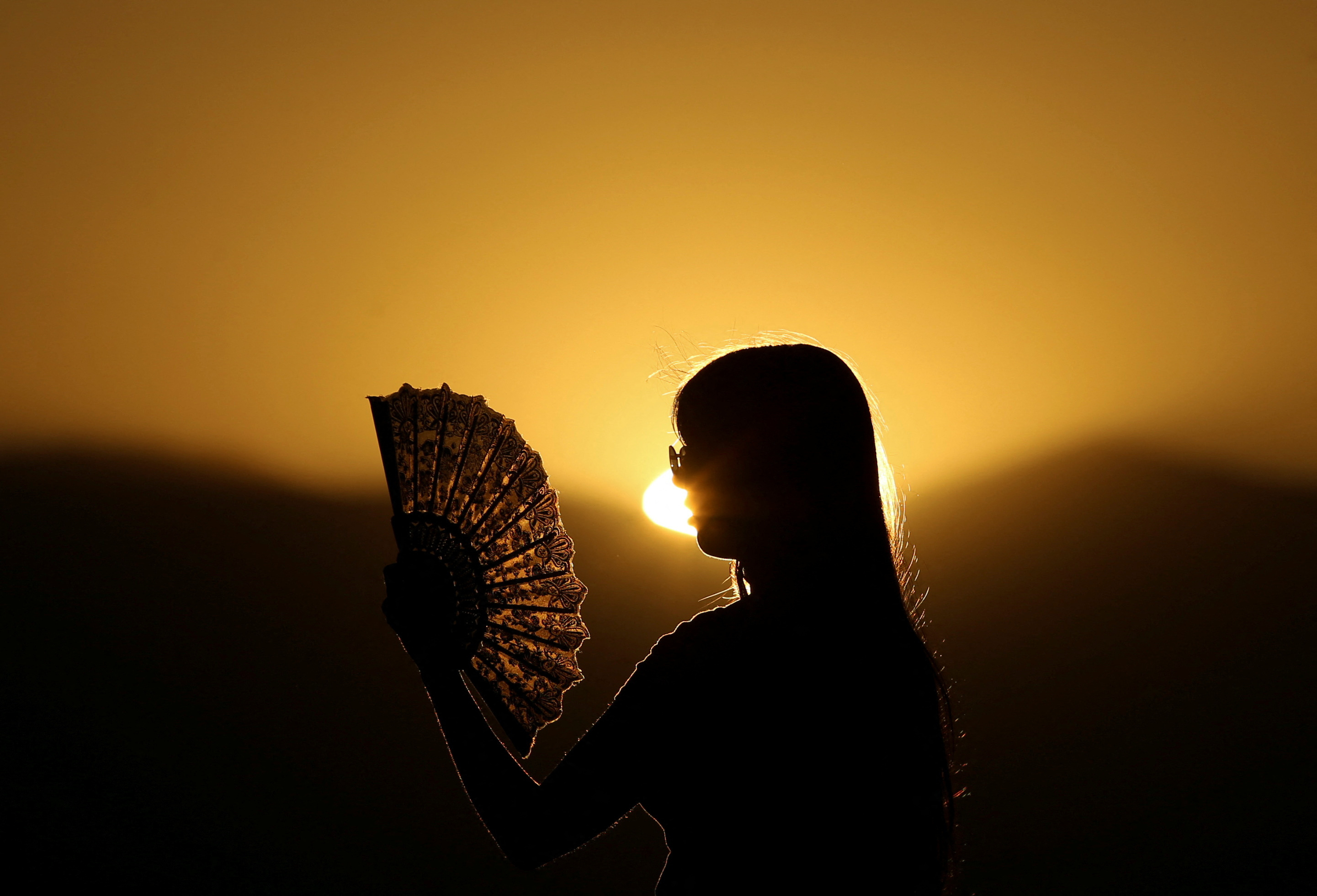 A girl cools off from the heat with a paper fan in Skopje