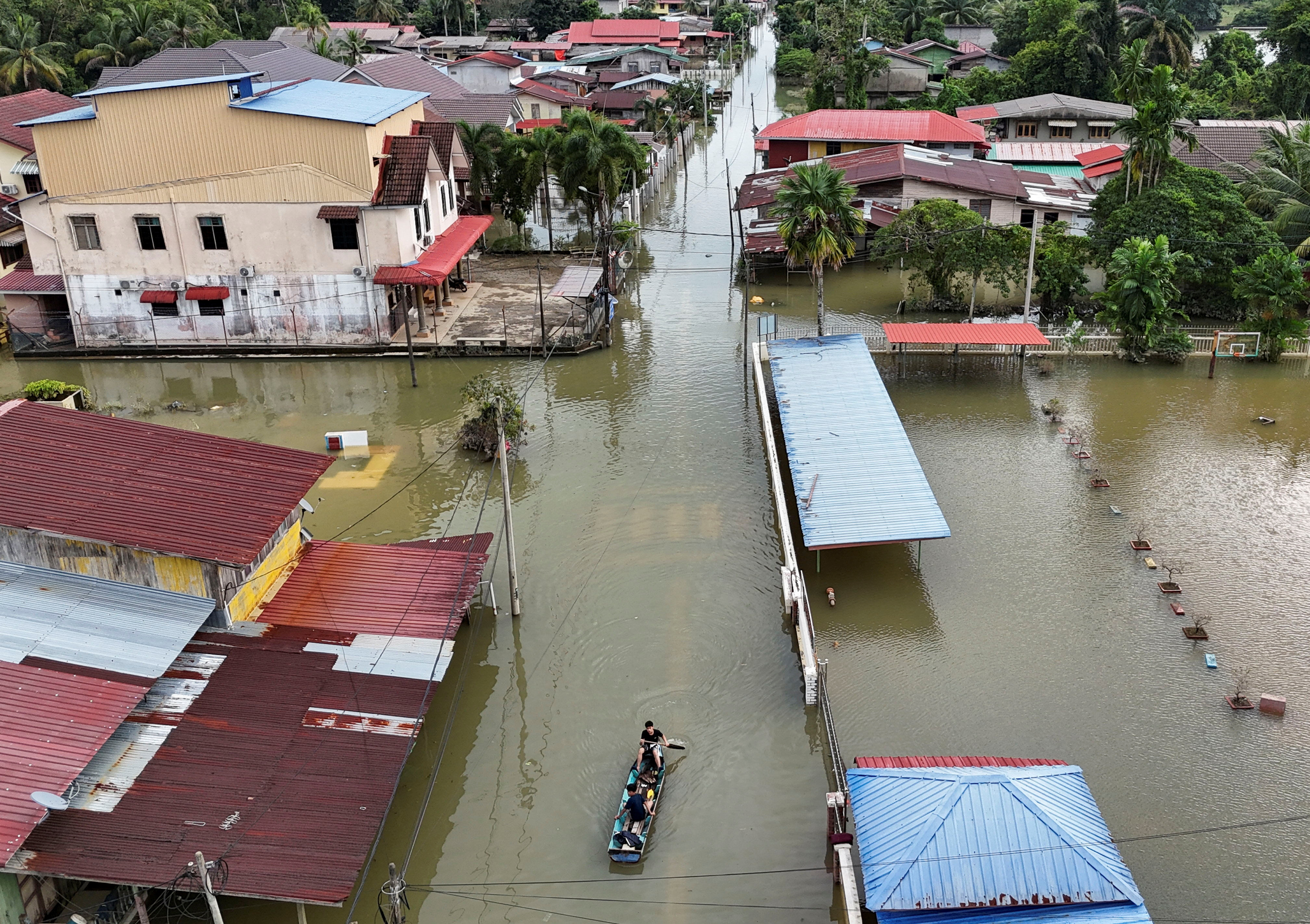 A drone view shows people riding boats in a flooded residential area in Rantau Panjang