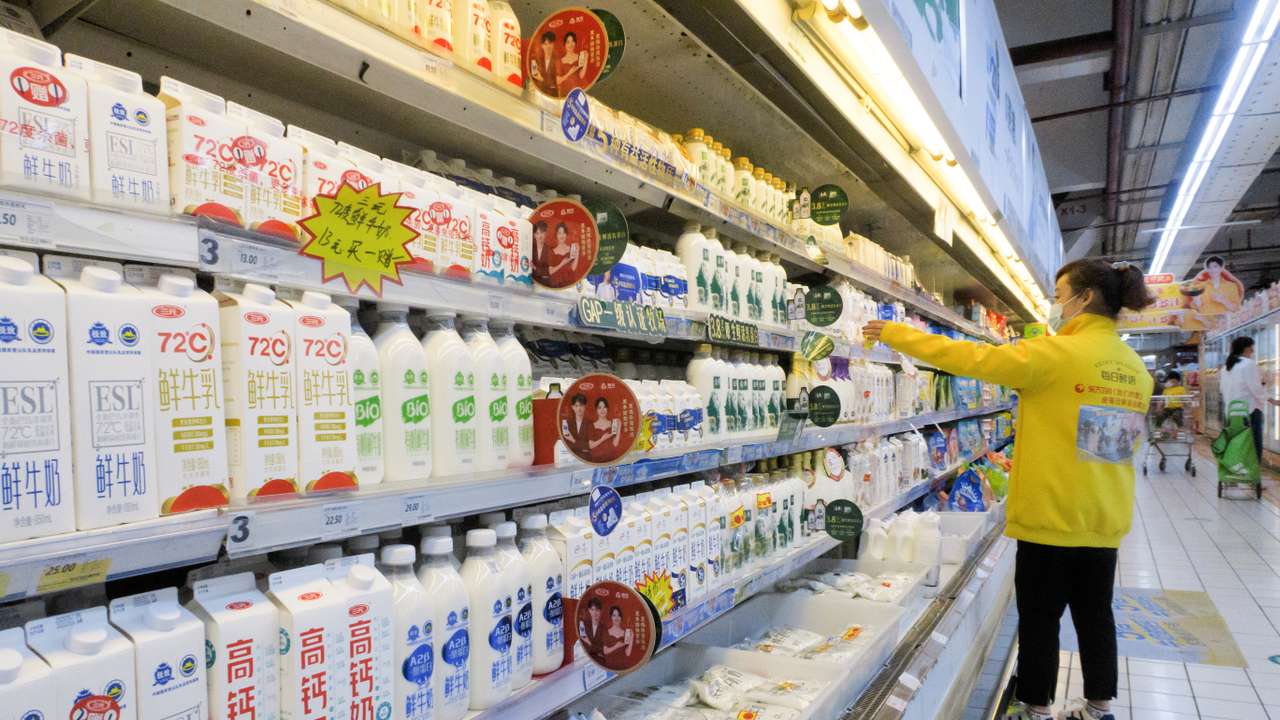 Staff member arranges cartons of milk on refrigerator shelves at a supermarket in Beijing