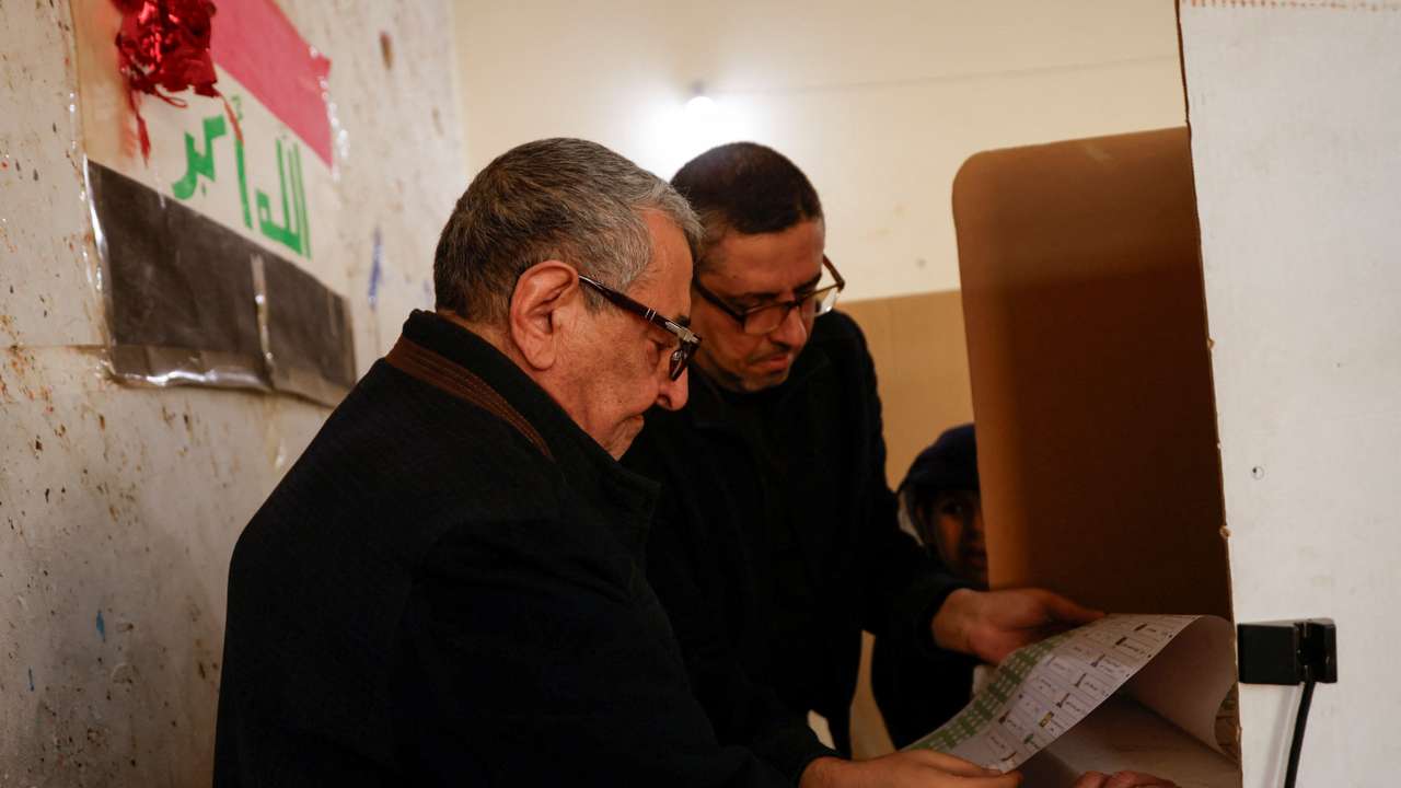 A relative helps an old Iraqi man as he votes during Iraq's provincial council elections, at a polling station in Baghdad