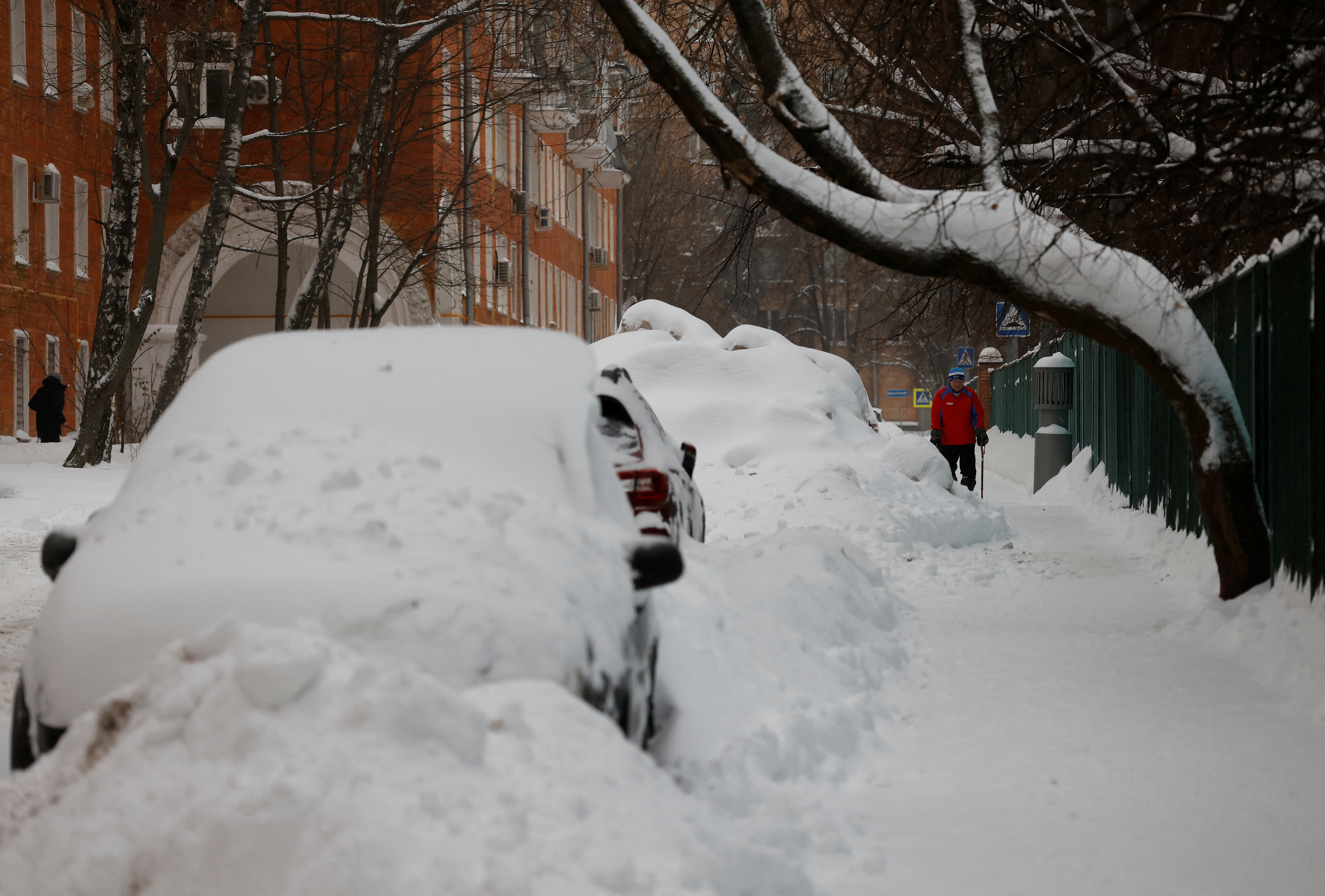 A man walks past cars covered with snow after heavy snowfall in Moscow