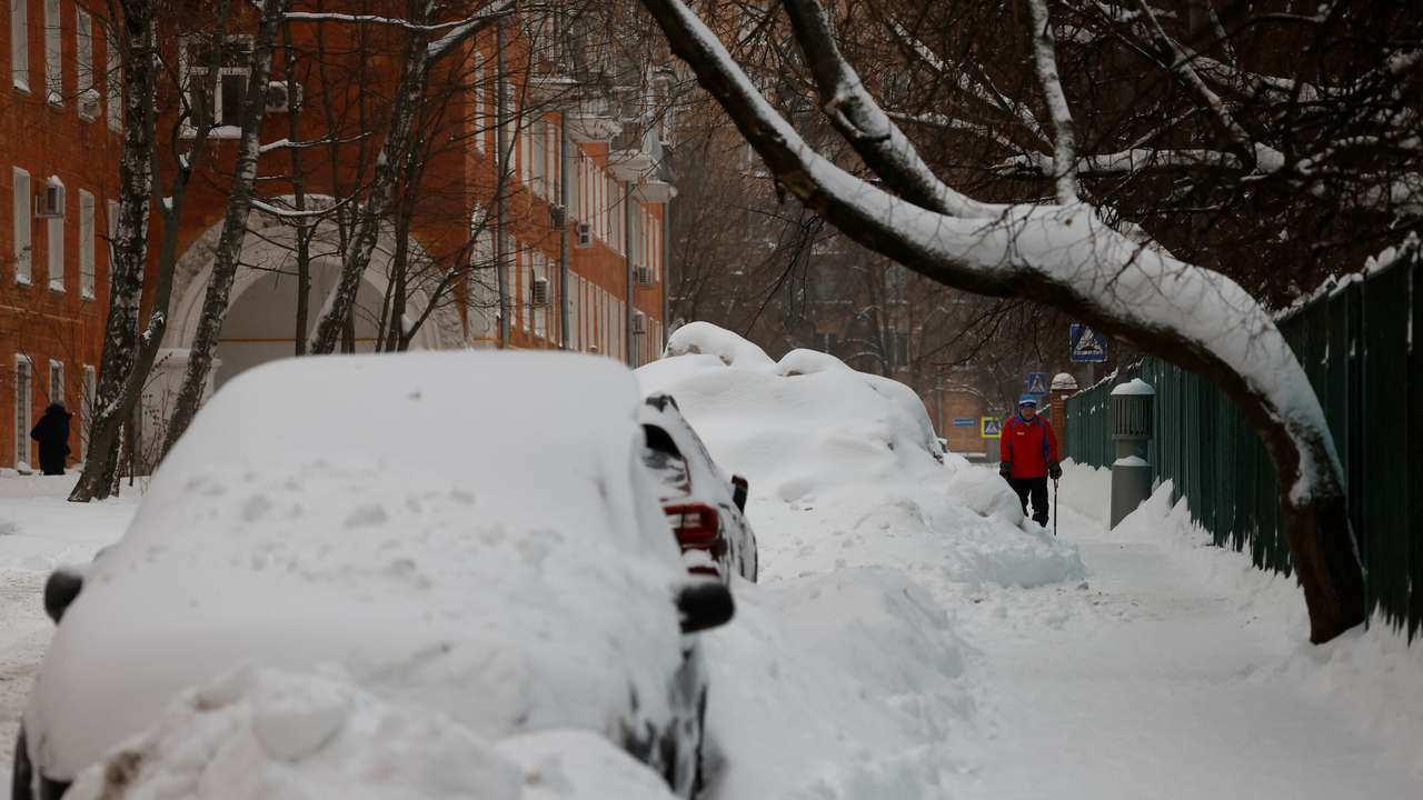 A man walks past cars covered with snow after heavy snowfall in Moscow