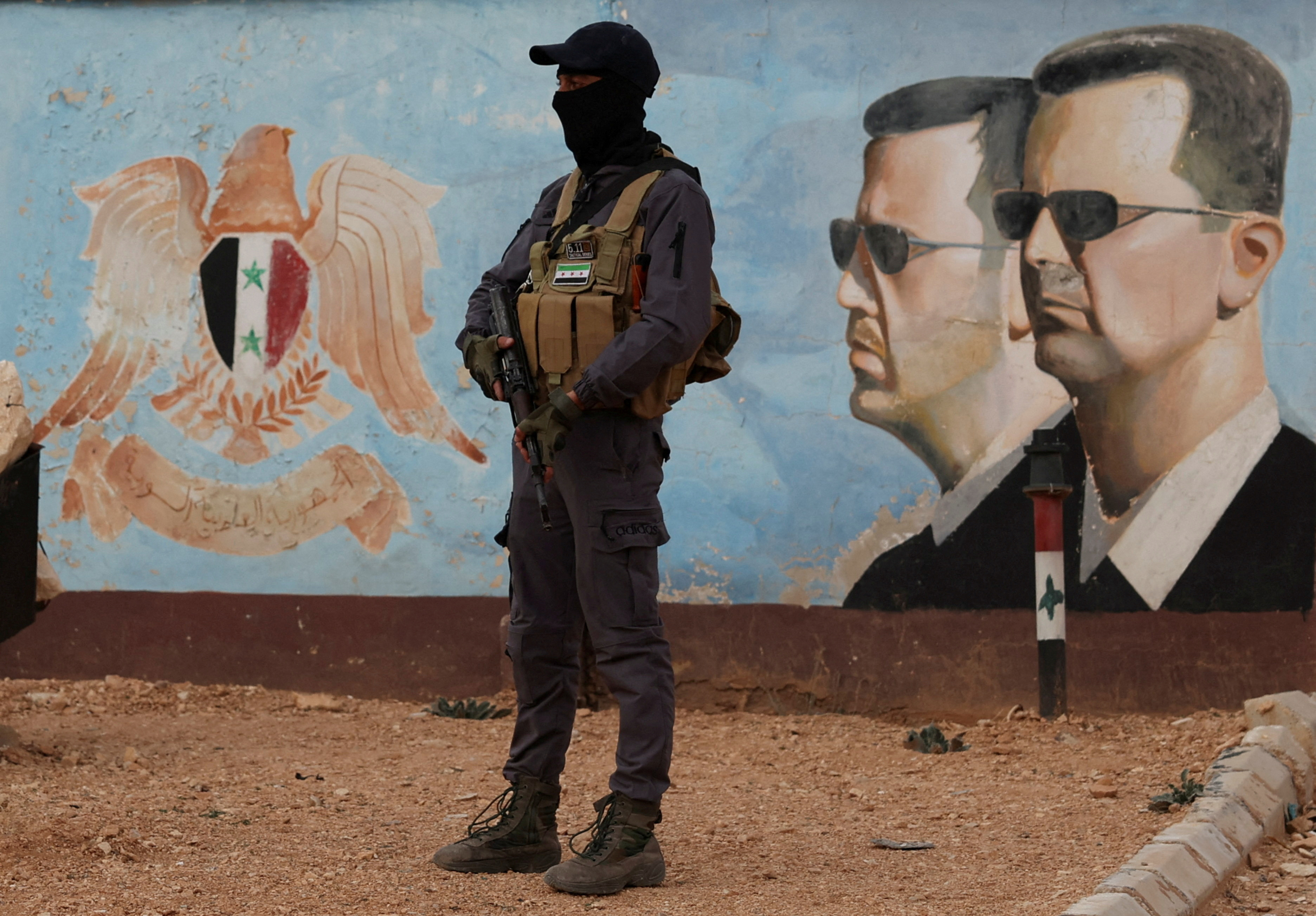 FILE PHOTO: A member of the former rebel group Hayat Tahrir al-Sham stands guard near an image of Syria's Bashar al-Assad at the fourth division headquarters in Damascus