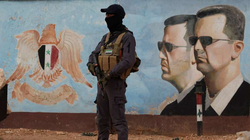 FILE PHOTO: A member of the former rebel group Hayat Tahrir al-Sham stands guard near an image of Syria's Bashar al-Assad at the fourth division headquarters in Damascus