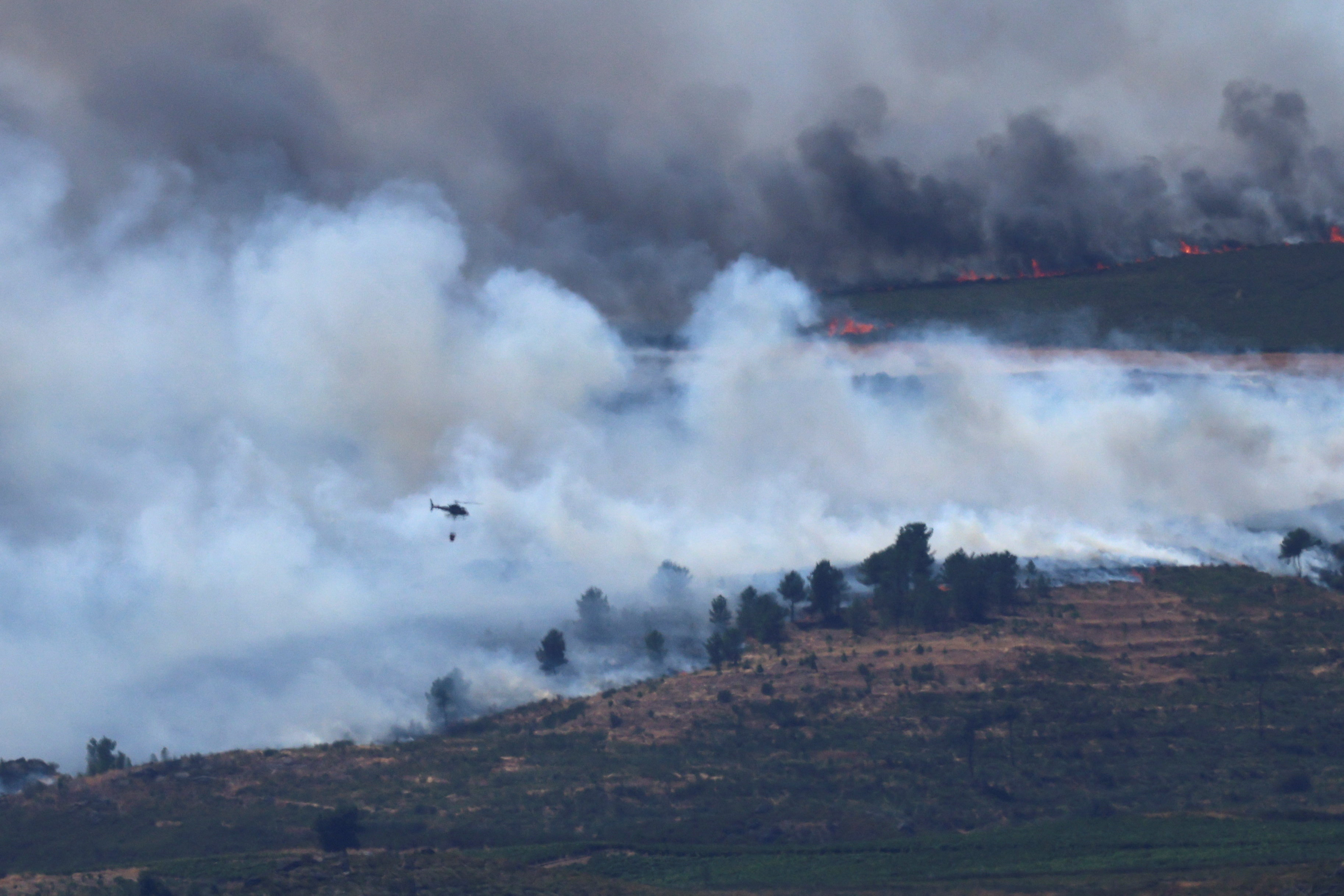 Smoke rises as a helicopter flies to combat a wildfire in the mountains of Oimbra