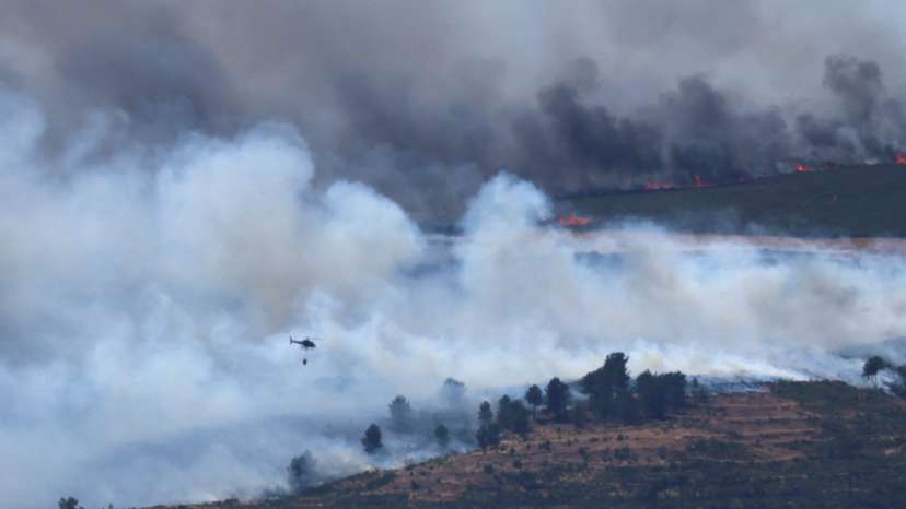 Smoke rises as a helicopter flies to combat a wildfire in the mountains of Oimbra